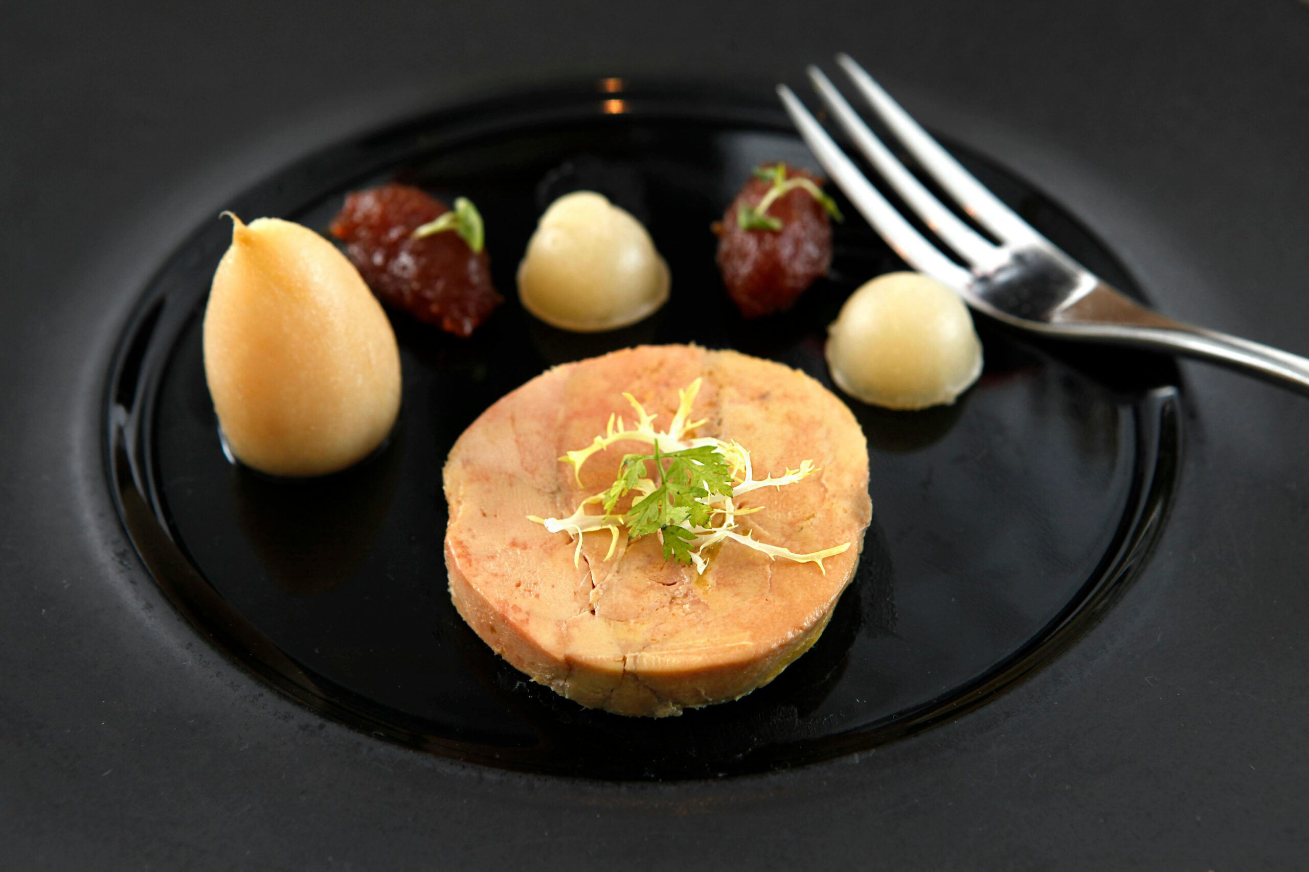 Delicate foie gras served on a black ceramic plate with garnish and puree accompaniments.